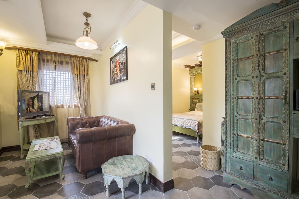 A room with a brown leather sofa, a green table, a television, and a green cabinet.