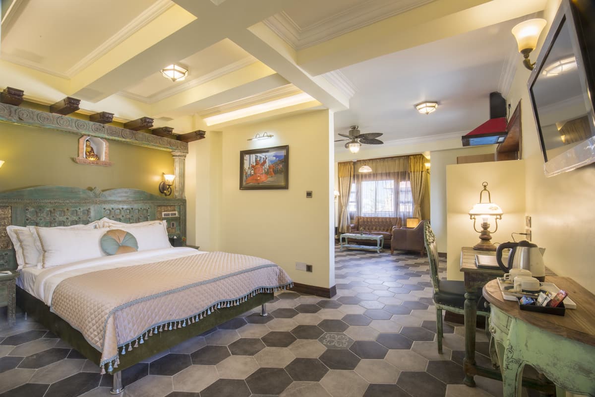 A hotel room with a large bed, a desk with a lamp, a chair, and a ceiling fan.
