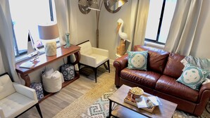 A living room with a brown leather sofa, a white armchair, a wooden coffee table, and a patterned rug. - Perfect Summer backyard, Steps to Beach, Bikes, boogie-board, bunk beds, Grill (St Augustine)