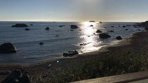 A coastal scene with the sun reflecting off the water, rocks, and a sandy beach.