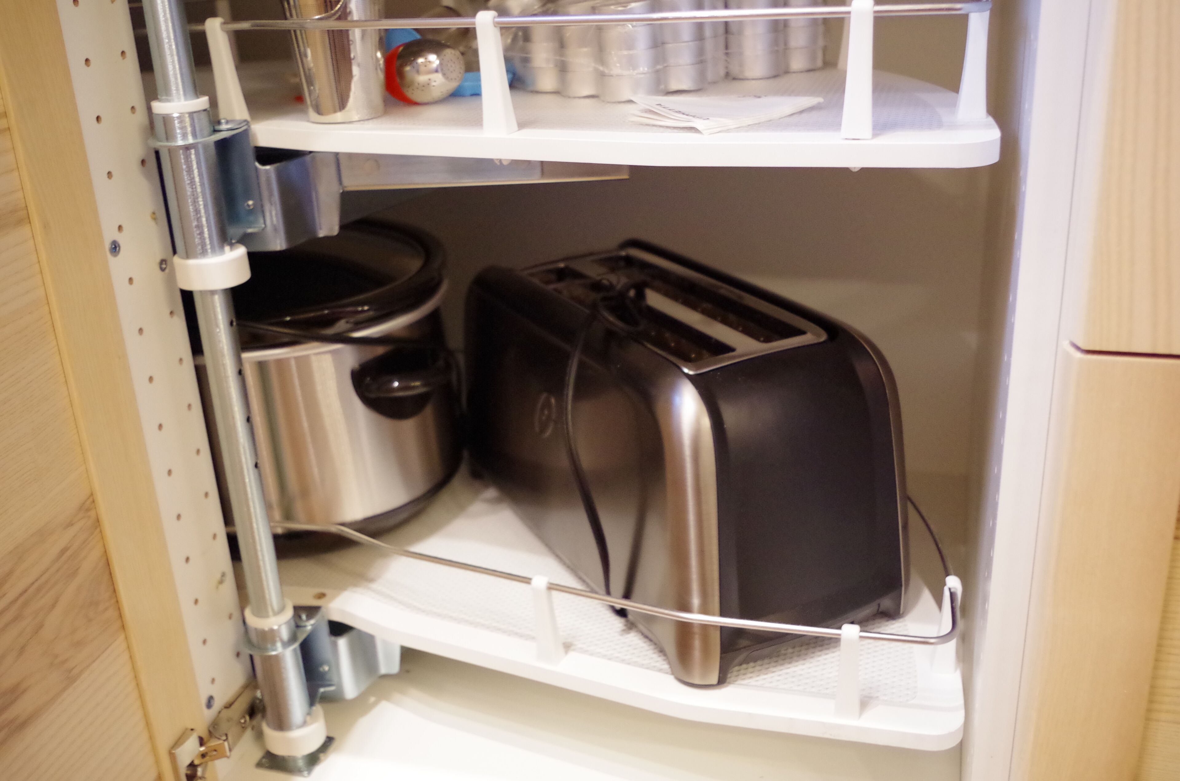A kitchen with a built-in toaster and a kettle on a shelf.