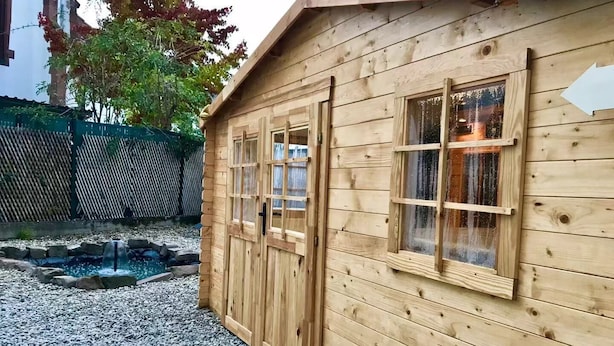 A wooden cabin with two windows and a door, surrounded by a gravel path and a small pond. - Appartement aux Deux Cigognes (Gries)
