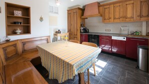 A kitchen with wooden cabinets, a dining table with a striped tablecloth, and a built-in oven. - Appartement aux Deux Cigognes (Gries)