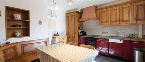 Une cuisine avec des meubles de rangement en bois, une table à manger recouverte d’une nappe à rayures et un four encastré.