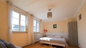 A bedroom with a bed, a radiator, a window with curtains, a bedside lamp, a wardrobe, and a painting on the wall. - Appartement aux Deux Cigognes (Gries)