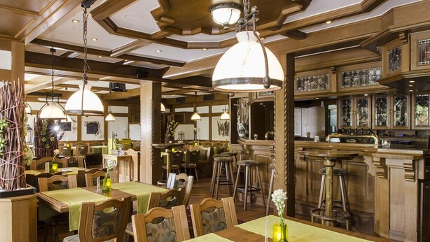 Un restaurant avec des meubles en bois, des lampes suspendues et un coin bar doté de tabourets.