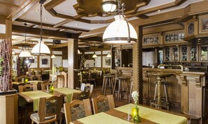Ein Restaurant mit Holztischen, hängenden Pendelleuchten und einer Bar mit Hockstühlen.