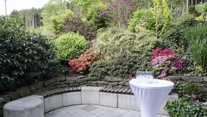 Un jardin agrémenté d’un banc en pierre et d’une table blanche, entouré de différentes plantes et fleurs.