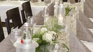 Une table élégamment dressée, ornée d’un centre de table composé de fleurs blanches et de verdure, entourée de verres à vin et d’une bougie.