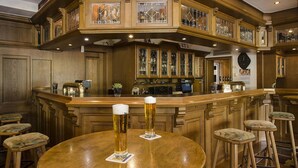 Un espace bar avec des comptoirs en bois, des tabourets et deux verres de bière posés sur une table ronde.