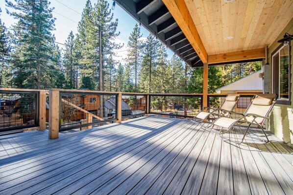 A wooden deck with a glass railing, outdoor chairs, and a view of a forested area.