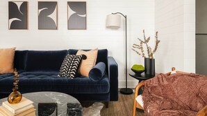 A living room with a dark blue sofa, a round coffee table, and three abstract wall art pieces.