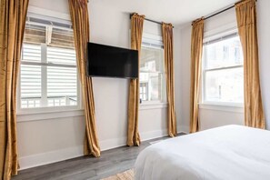 Ein Hotelzimmer mit Bett, flachbildfernseher an der Wand und großen Fenstern mit Vorhängen.