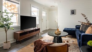 A living room with a flat-screen TV, a ceiling fan, a dark blue sofa, and a coffee table.