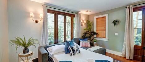 A bedroom with a bed, bedside tables, a window with curtains, and a potted plant.