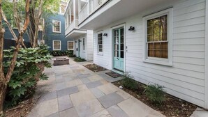 A two-story house with a covered porch, a front door, and a small front yard with a stone pathway. - Monaco Manor | Charleston Home w/ Rooftop Deck! (Charleston)