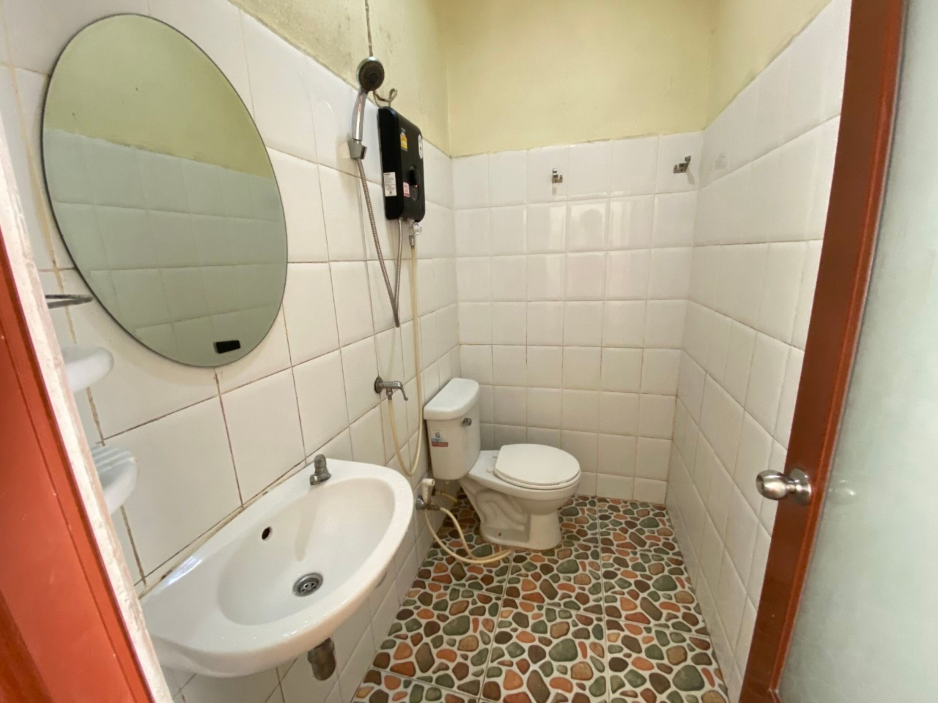 Un baño pequeño con lavamanos, inodoro y ducha blancos. El piso presenta un diseño de mosaico.