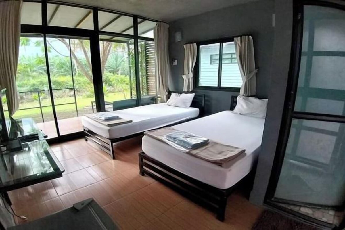 A room with two beds, a desk, and large windows.
