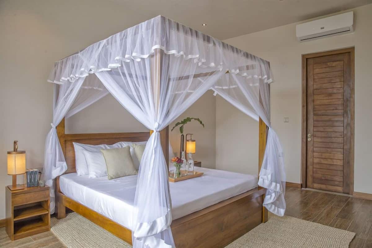 A four-poster bed with a canopy, bedside lamps, a wooden nightstand, and a wooden door.