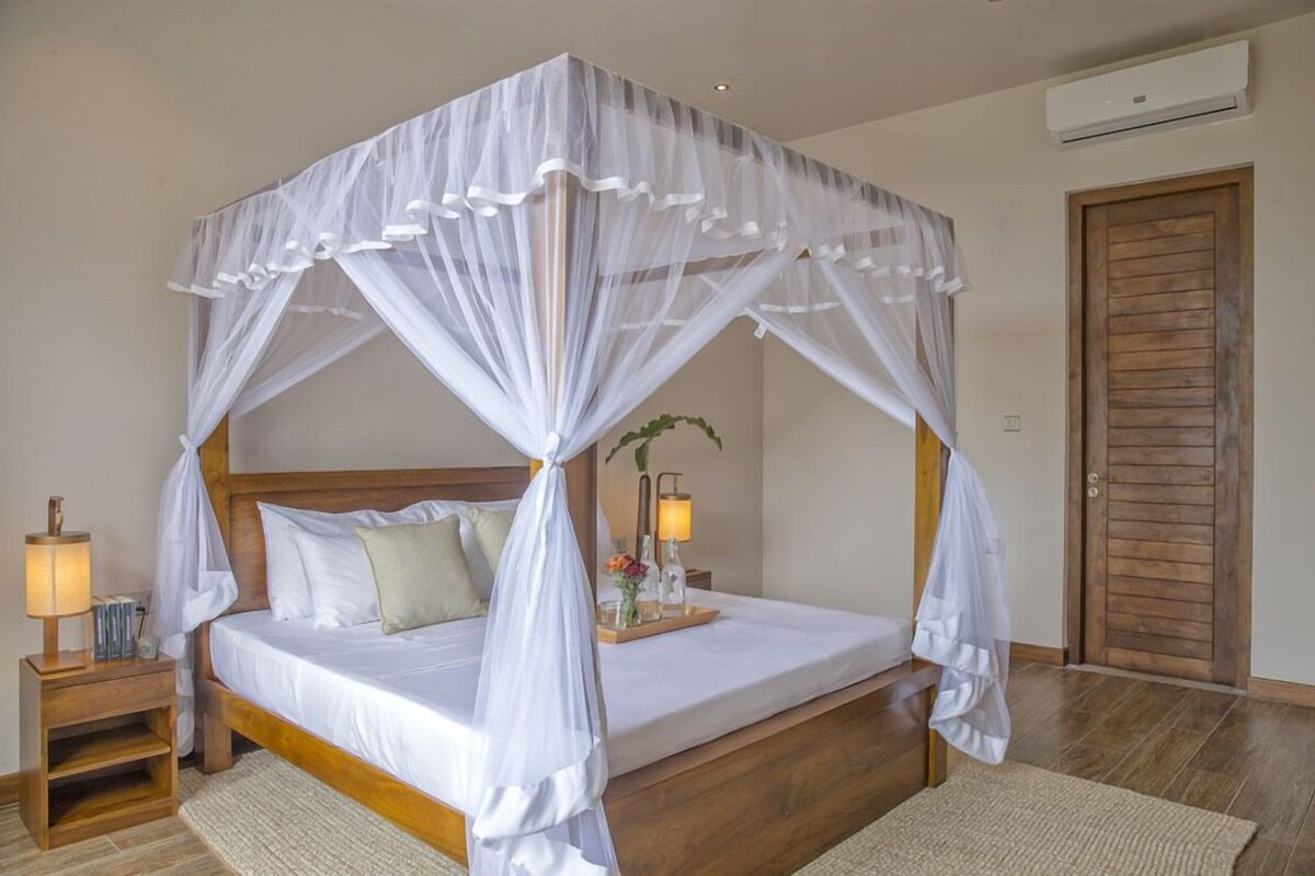 Una cama con dosel, lámparas de noche, una mesita de madera y una puerta de madera.