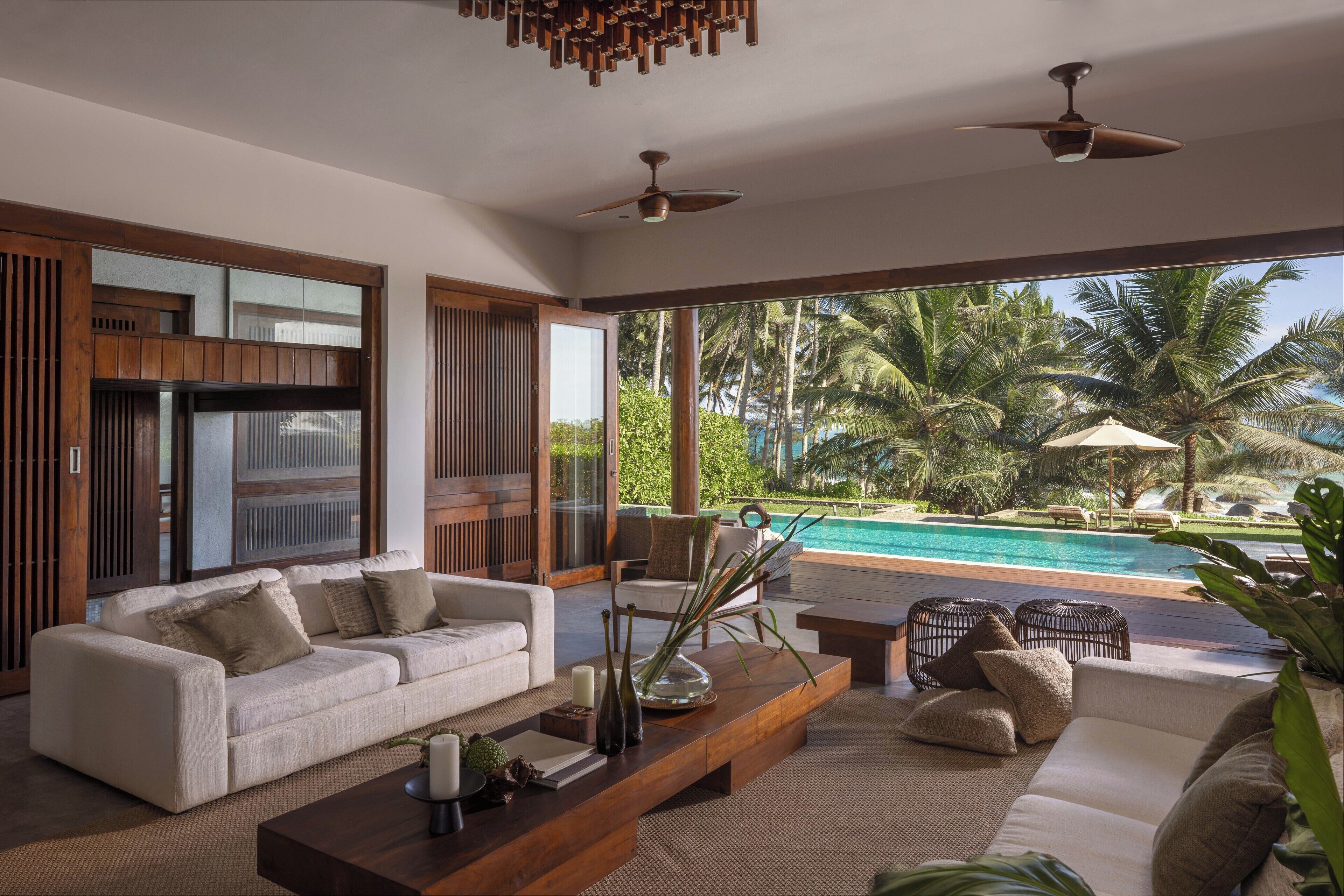 A modern living room with a sofa, coffee table, and a view of a pool and palm trees.