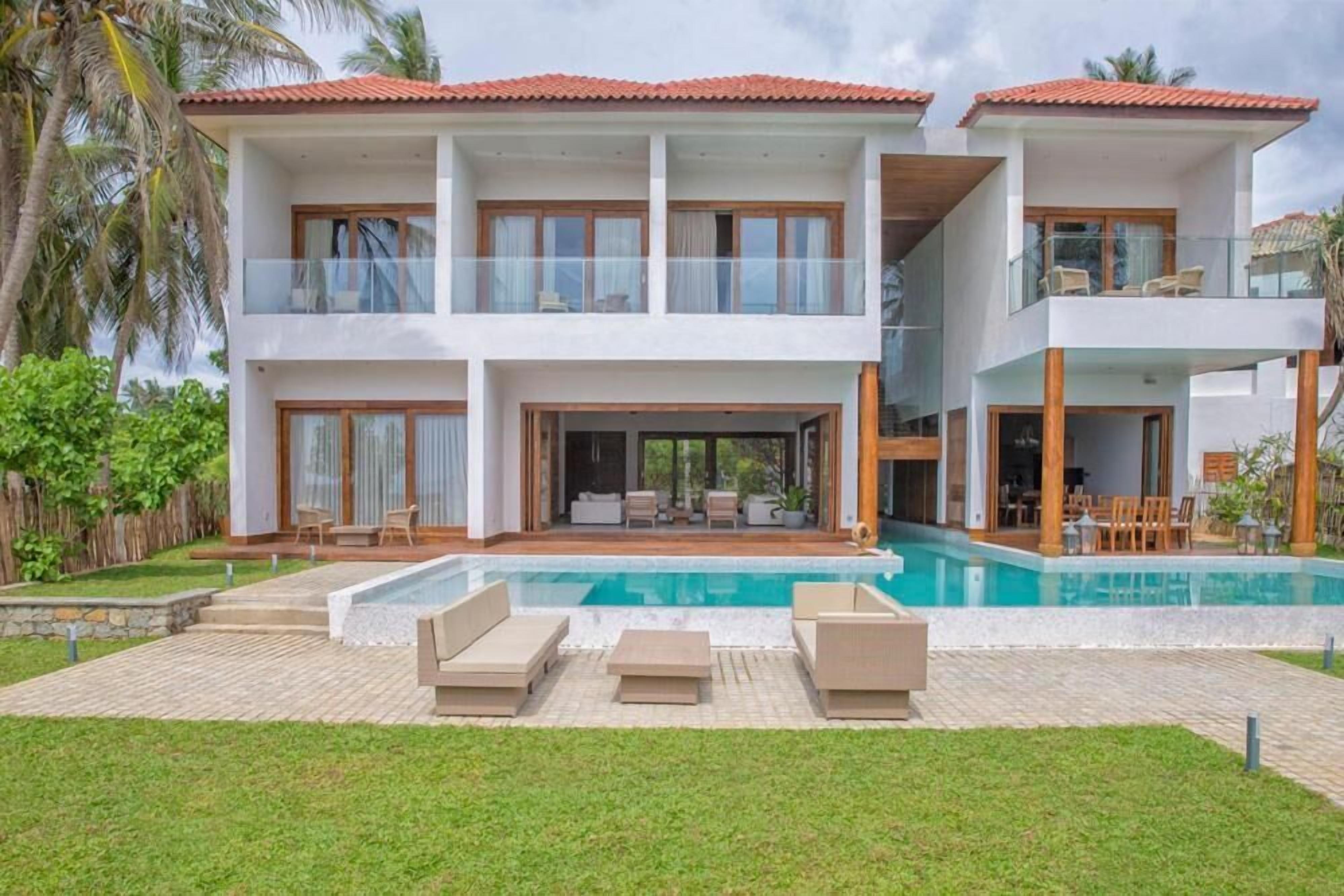 Una casa de dos pisos con piscina, mobiliario exterior y un césped bien cuidado.