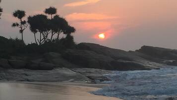A beach with a sunset, rocky shoreline, and sparse vegetation.