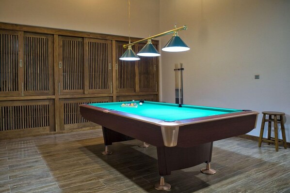 A pool table with a green felt surface, wooden cabinets, and a stool.
