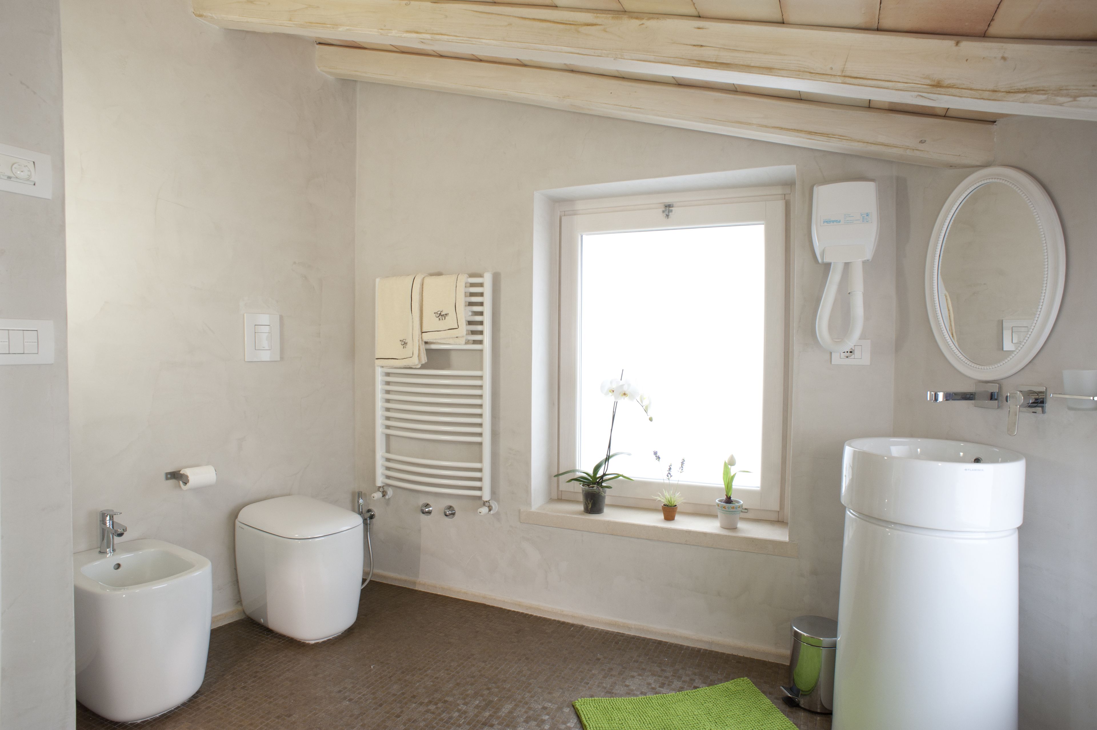 Een badkamer met toilet, bidet, wastafel, spiegel, raam en handdoekrek.