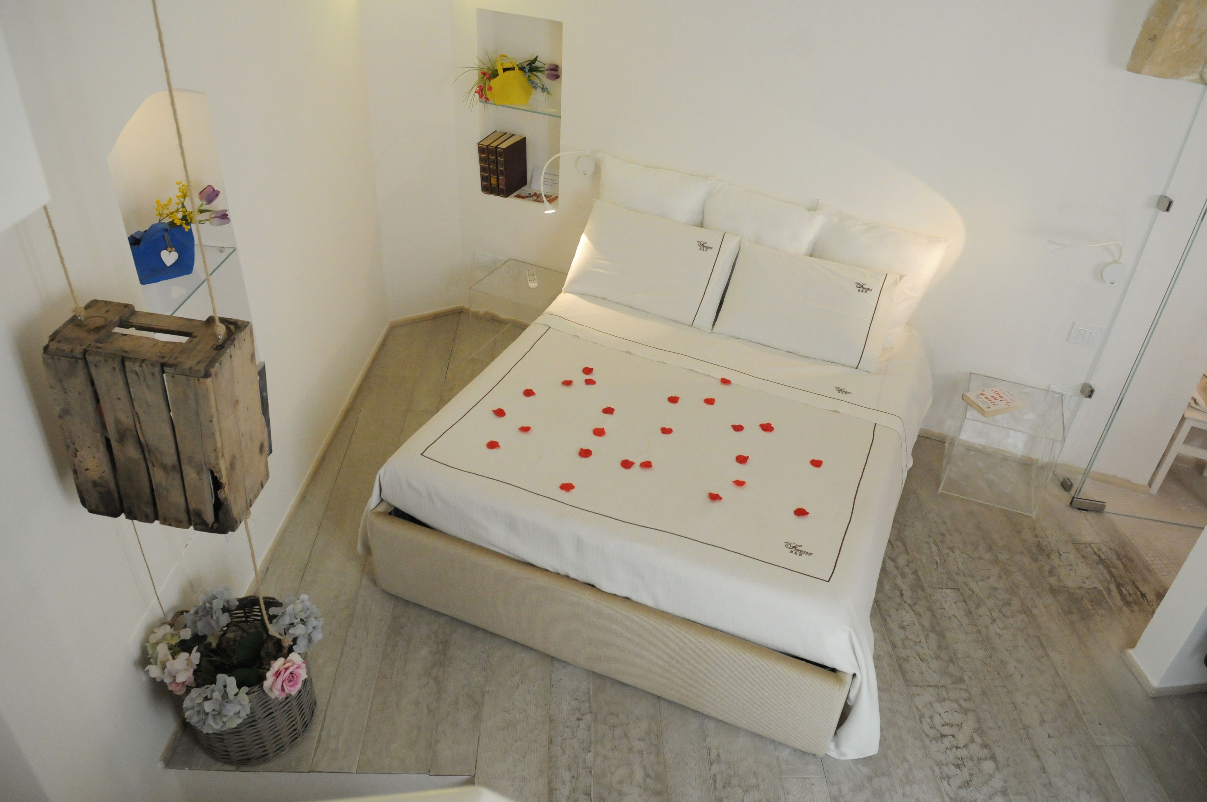 Una camera da letto ordinata con un letto, comodini, una scatola di legno appesa e un piccolo ripiano con oggetti decorativi.