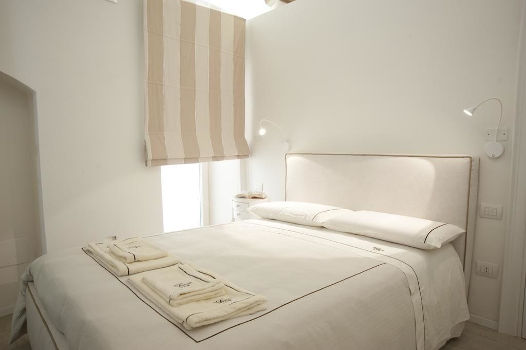 A hotel room with a large bed, a bedside table, a lamp, and a window with a striped blind.