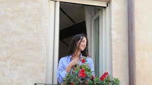Iemand staat op een balkon met een raam, met een bloemenmand in de hand.