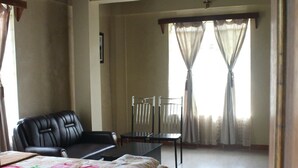 A hotel room with a bed, a chair, a small table, and a window with curtains. - Pumpkin StreamSide Guest House (Shillong)