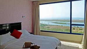 A bedroom with a large window offering a view of a body of water and landscape. - Le Temps Perdu (Oualidia)