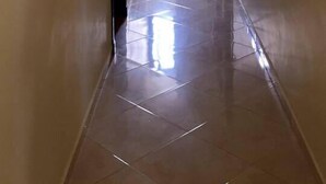 A hallway with a tiled floor, a vase with flowers, and a window at the end. - Le Temps Perdu (Oualidia)