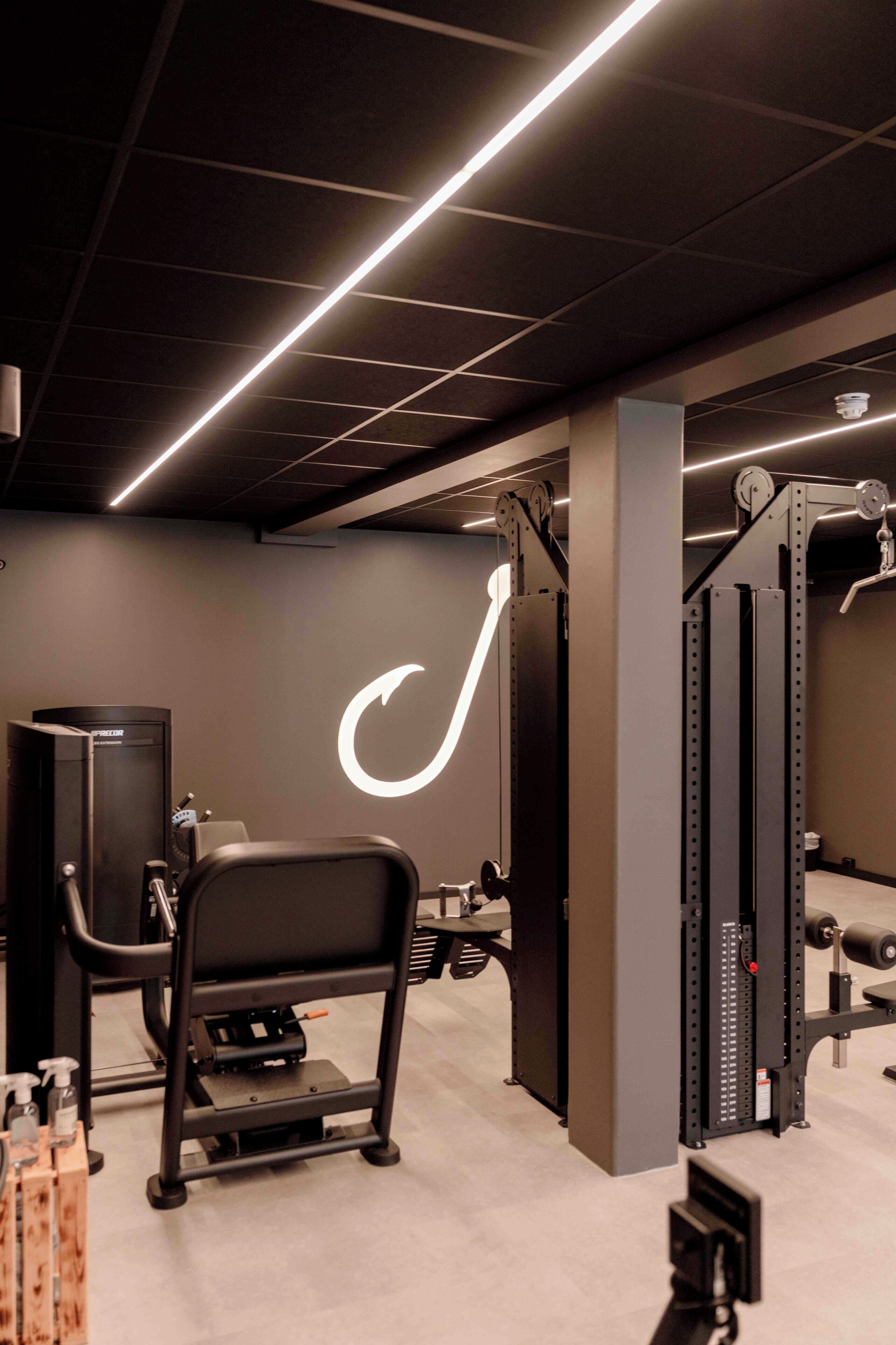 A gym with weightlifting equipment, a wall-mounted logo, and a ceiling with linear lights.