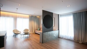 A modern hotel room with a wooden floor, a sofa, two armchairs, a desk, and a large window with curtains. - Stad Hotell (Stad)