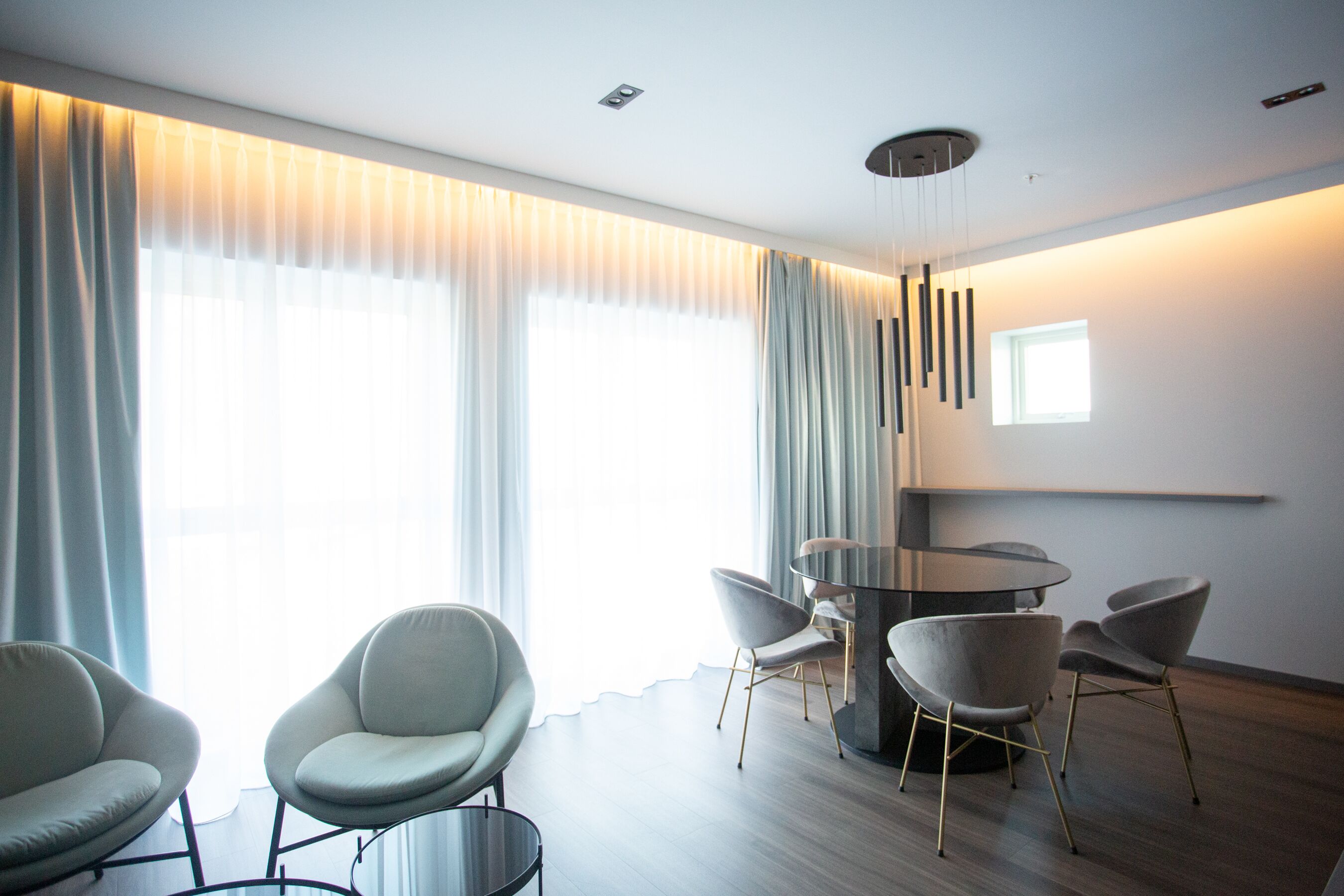 Un'area pranzo moderna con un tavolo rotondo e quattro sedie, ampie finestre con tende leggere e un design minimalista del soffitto.