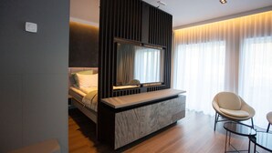 A modern hotel room with a bed, a built-in TV, a seating area, and large windows. - Stad Hotell (Stad)