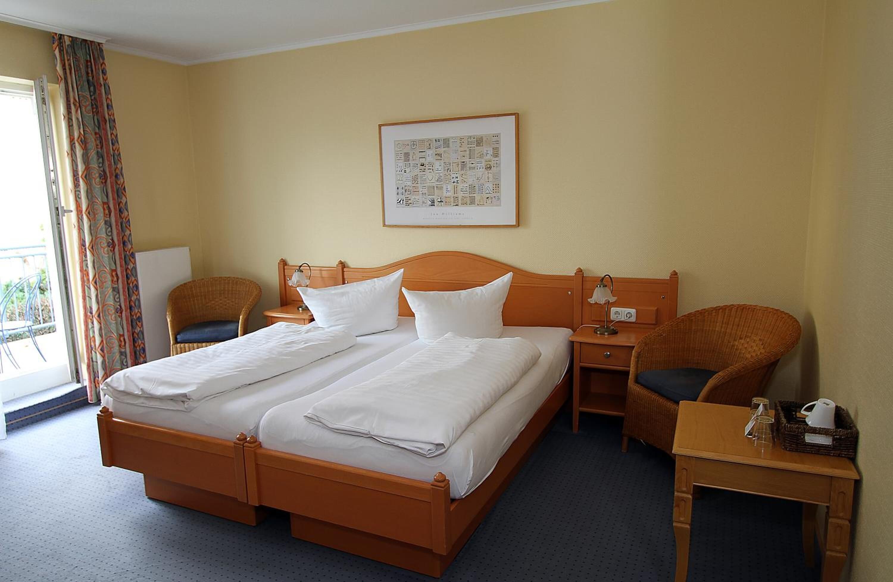 A hotel room with a double bed, two bedside tables, a chair, a small table, and a window with curtains.
