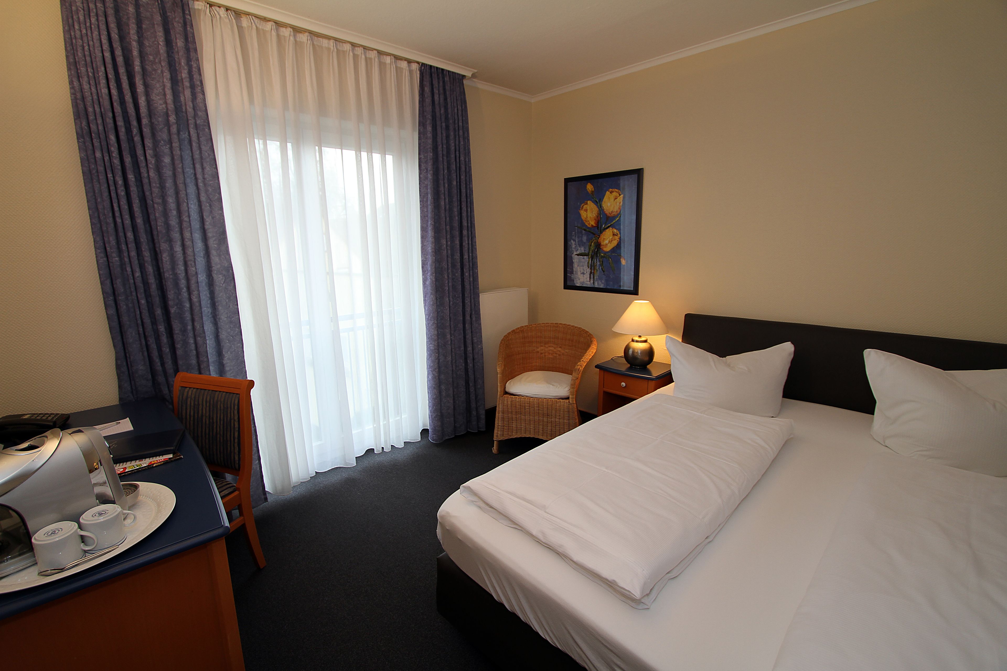 Une chambre d’hôtel comprenant un lit, un bureau avec une machine à café, une chaise et une lampe.