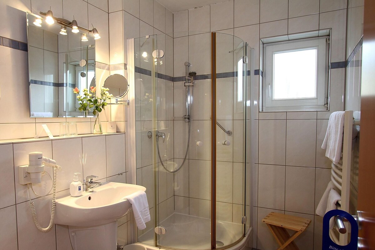 A modern bathroom with a glass-enclosed shower, a sink with a towel, and a mirror above the mirror.