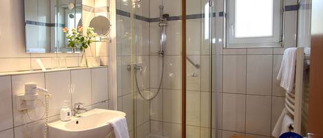 A modern bathroom with a glass-enclosed shower, a sink with a mirror, and a small wooden stool.