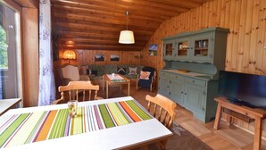 L’intérieur chaleureux d’un chalet comprend une table à manger, des chaises, un canapé, un fauteuil à bascule, un téléviseur et des armoires en bois.