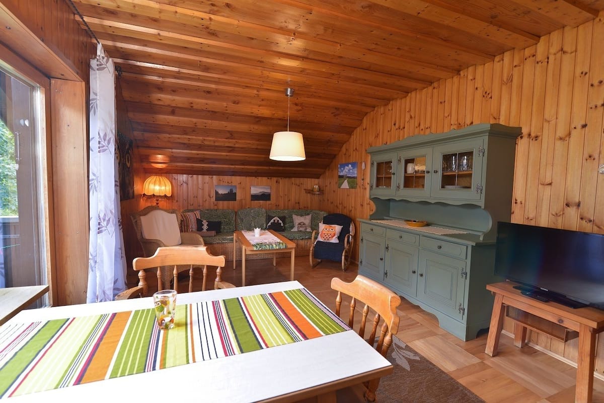 Un interior de cabaña acogedor con una mesa de comedor, sillas, un sofá, un sillón mecededor, un televisor y armarios de madera.