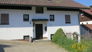 A white building with a tiled roof, a black door, and a small garden with yellow flowers.