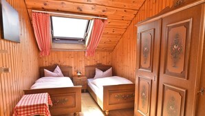 A wooden cabin bedroom with two beds, a small table, and a wardrobe.