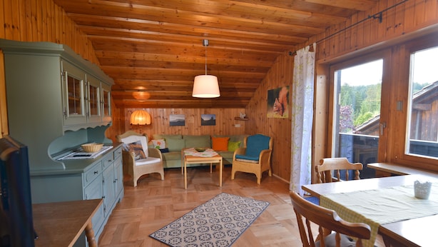 A cozy cabin interior with wooden walls, a dining table, a sofa, and a kitchen area.