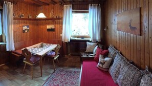 Interior acogedor de una cabaña con una mesa de comedor de madera, sillas, un sofá y un radiador.