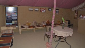 A room with a pink ceiling, a bench with cushions, a small table with a vase, and a poster on the wall. - The Chirag Desert Camp Sam Sand Dunes (Jaisalmer)